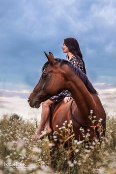 a woman riding on the back of a brown horse in a field full of flowers