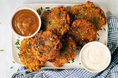 some fried food on a white plate with sauces and a blue striped towel next to it