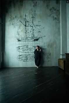 a person standing in front of a wall with writing on it and a ship drawn on the wall