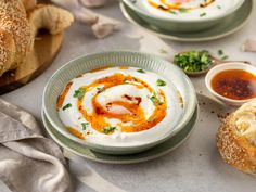 two bowls of hummus, bread and sauce on a table with other food items