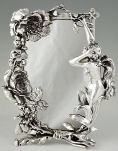 an ornate silver frame with flowers and leaves on it's sides, in front of a mirror