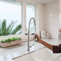 a woman is washing her hands under the faucet in front of a window