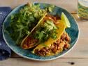 two tacos on a plate with guacamole and salsa next to a glass of water