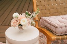 a vase with flowers sitting on top of a white table next to a wooden chair