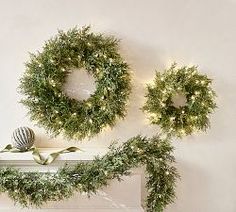 two wreaths on top of a mantle with lights around them and one hanging from the mantel