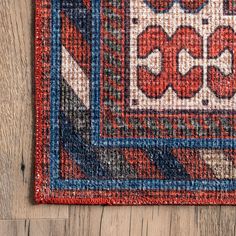 a red, blue and white rug on a wooden floor with wood planks in the background