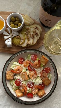 a plate with shrimp, lettuce and tomatoes on it next to two bottles of wine