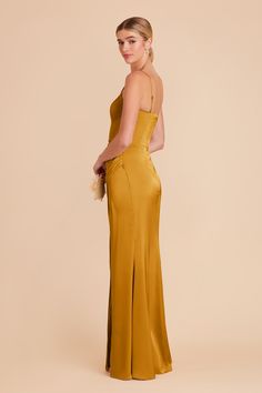 the back of a woman wearing a mustard colored evening gown, with her hands in her pockets