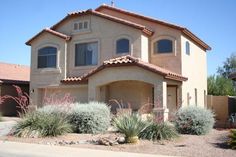 a large house in the middle of a desert with plants and shrubs around it's corner