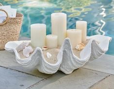 some candles are sitting on the edge of a pool near a basket with seashells