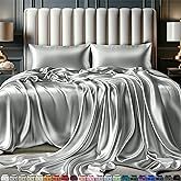 a large bed covered in silver sheets and pillows next to two night stands with lamps on either side