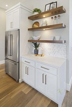 a kitchen with white cabinets and open shelving on the wall, along with a stainless steel refrigerator