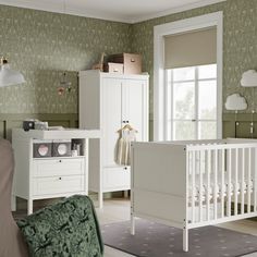 a baby's room with green wallpaper and white furniture