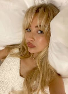 a blonde woman laying in bed with white sheets and pillows on top of her head