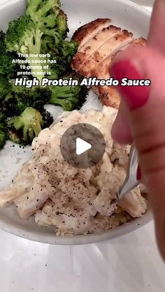 a person is eating broccoli and chicken with a knife in their hand on a white plate