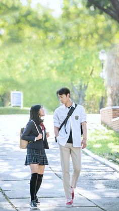 a young man and woman walking down a sidewalk together, one is talking to the other