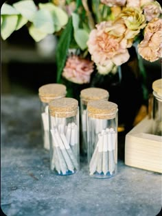 three glass jars filled with candles sitting on top of a table next to some flowers