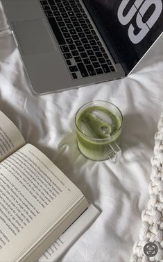 an open book sitting on top of a bed next to a cup of green liquid