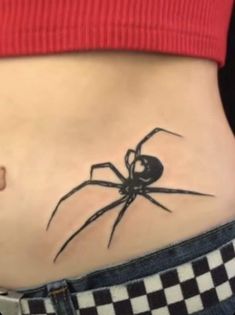 a woman's stomach with a black spider tattoo on her belly and checkered jeans