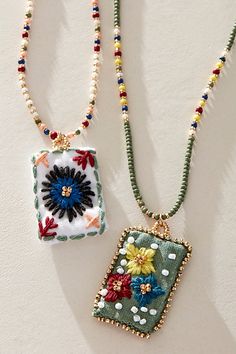 two beaded necklaces with flowers and beads hanging from the sides on a white surface