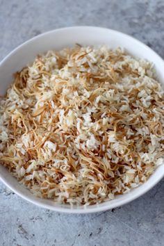 a white bowl filled with shredded rice on top of a gray counter next to a cup