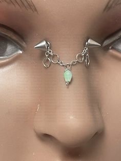 the face of a mannequin is adorned with silver spikes and a green stone