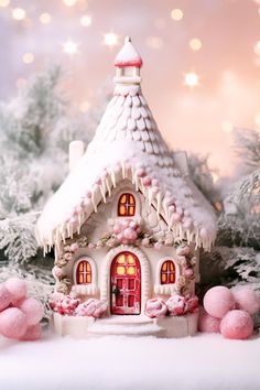 a small white house with pink pom poms on the ground in front of snow covered trees