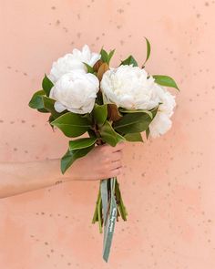 a bouquet of white flowers being held by a woman's hand against a pink wall