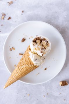 an ice cream cone with walnuts on top sits on a white plate next to nuts