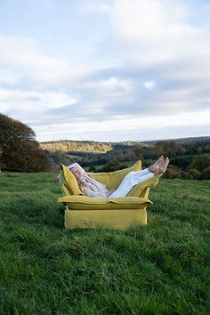 a person laying on top of a yellow chair in the grass with their feet up