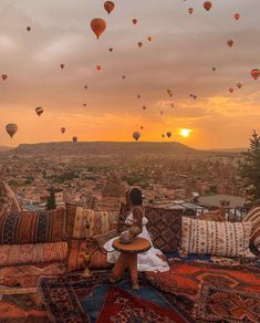 a woman sitting on top of a couch next to pillows and hot air balloons in the sky