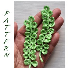 small crocheted flowers in the palm of someone's hand with green leaves