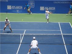 two men playing tennis on a blue and green court with other people in the background