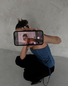 a woman kneeling down while taking a selfie with her cell phone in front of her