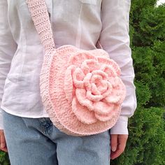 a woman holding a pink crocheted purse with a large flower on the front