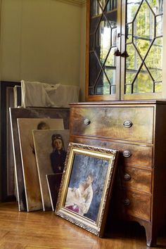 an old dresser with pictures on it in front of a mirror and other items sitting on the floor