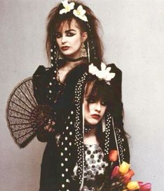 two women dressed in black and white with flowers on their head, holding parasols