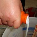 a person is pouring water into a white bowl with an orange sippy cup in it