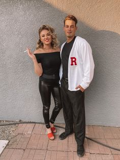 a man and woman standing next to each other in front of a wall with the letter r on it