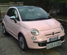 a small pink car parked in front of a fence