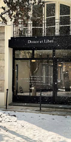 a store front with snow falling on the ground and windows covered in black glass,