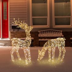 two lighted reindeer statues in front of a house