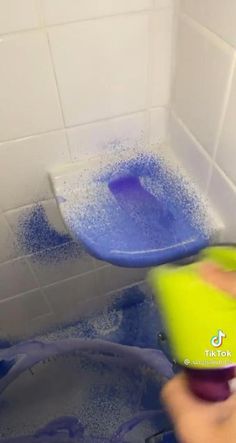 a person using a sponge to clean a bathtub with a blue and green plunger