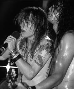 two men with long hair and tattoos on their arms are singing into microphones at a concert