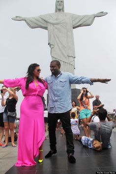 a man standing next to a woman in front of a statue with her arms outstretched