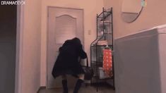 a woman in black coat and knee high boots walking into a room with an open door