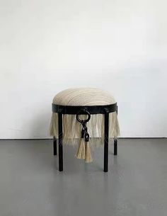 a small stool with tassels on it in front of a white wall and floor