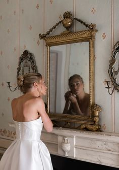 a woman in a wedding dress looking at herself in the mirror