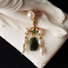 These dainty yet sumptuous earrings are a reproduction of an extant Roman pair dating from the 2nd to 3rd Century and housed at the Louvre Museum in Paris, France. Each earring consists of a gold plated bar, embellished with one green onyx and two freshwater pearl cabochons. From this are suspended two fresh water pearl pendants and a green jasper nugget bead. They have gold plated earring posts adorned with bezel set freshwater pearls. All the beads are natural and as such will have slight differences in shape and colour but any irregularities only serve to make these earrings look more authentically Roman! Limited edition design. Gold plated posts. Length (from top of earring fitting to bottom of earring) 4.2cm (1.65 inches). Please note: All photos are taken under natural light. However Roman Costume, Museum In Paris, Green Jasper, Louvre Museum, Earring Posts, Fresh Water Pearl, Pompeii, Green Onyx, Gold Plated Earrings