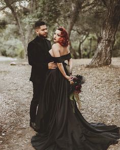 a man and woman standing next to each other in front of trees with leaves on the ground